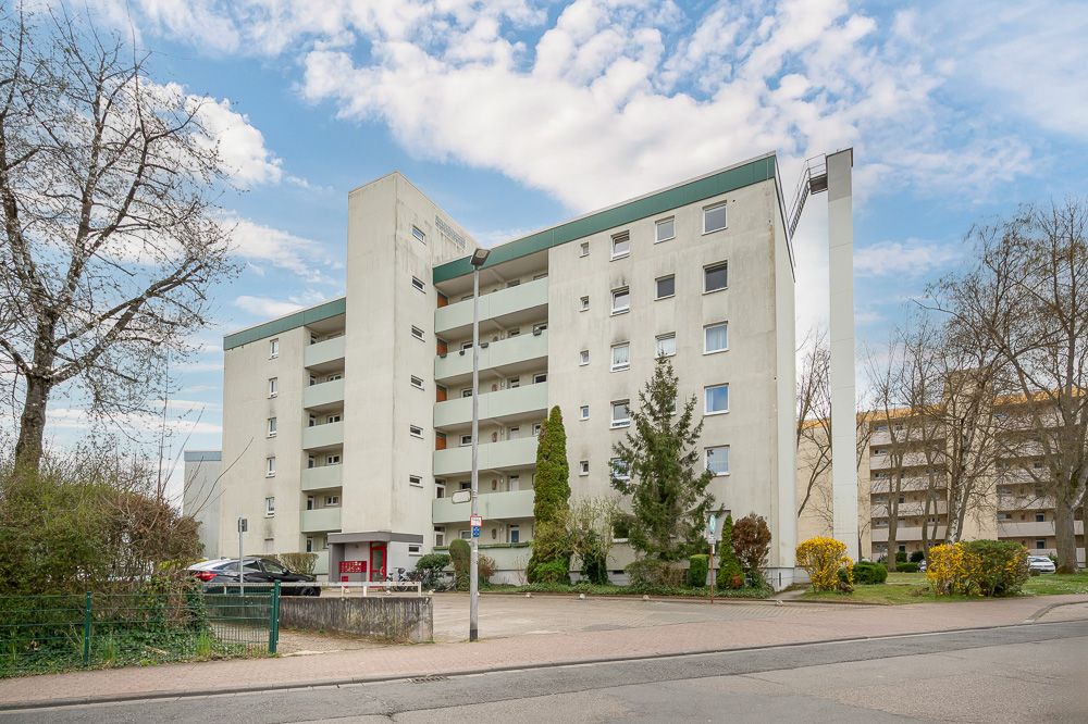 Mehrstöckiges Wohnhaus mit Balkonen und begrüntem Vorplatz.