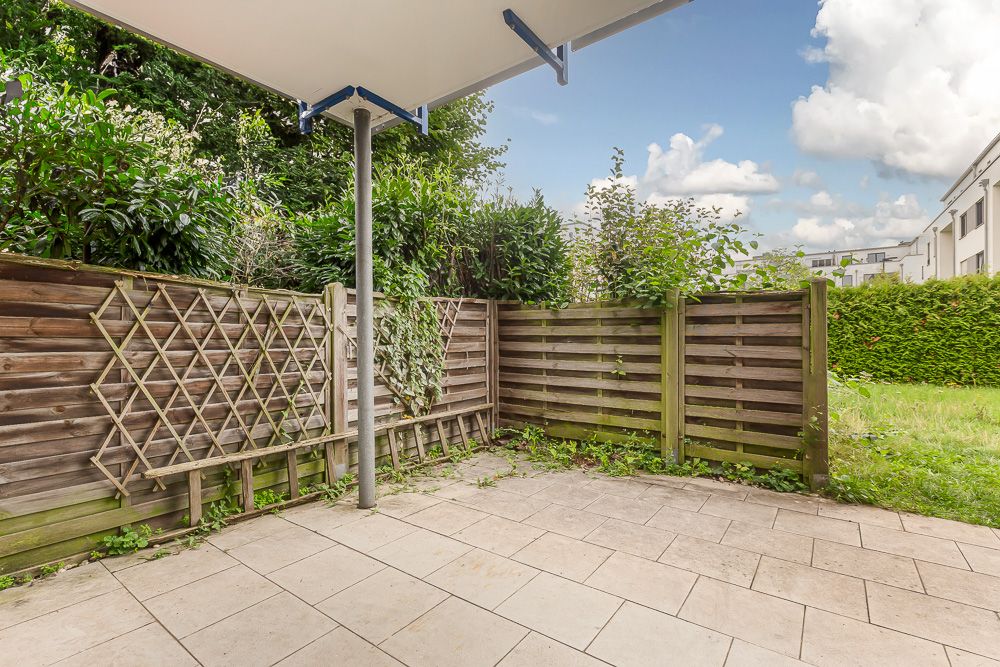 Geflieste Terrasse mit Holzzaun und Bewuchs im Gartenbereich eines Wohnhauses.