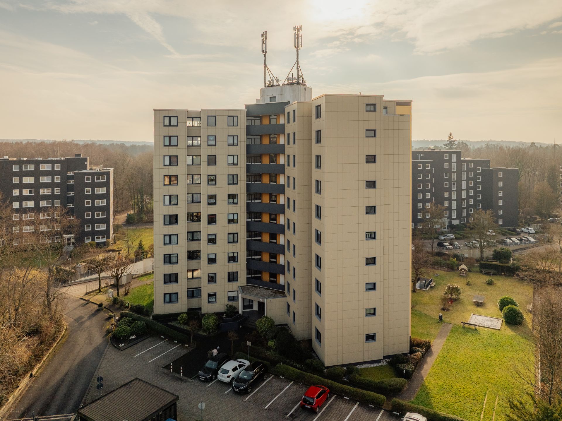 Mehrstöckiges Wohngebäude mit Parkplätzen und Grünfläche im Vordergrund.