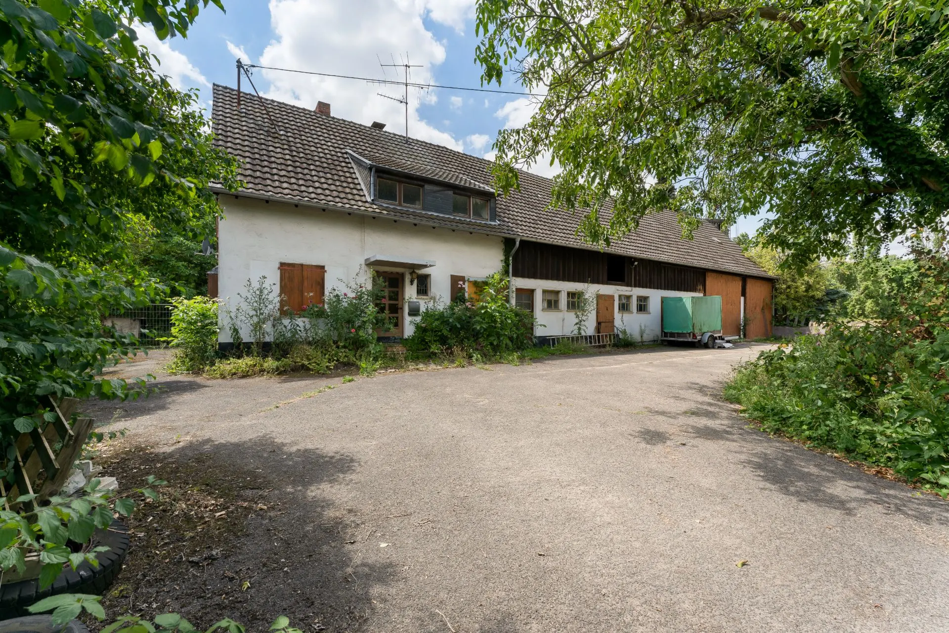 Großes Wohnhaus mit Satteldach und Hof, umgeben von Bäumen und Sträuchern.