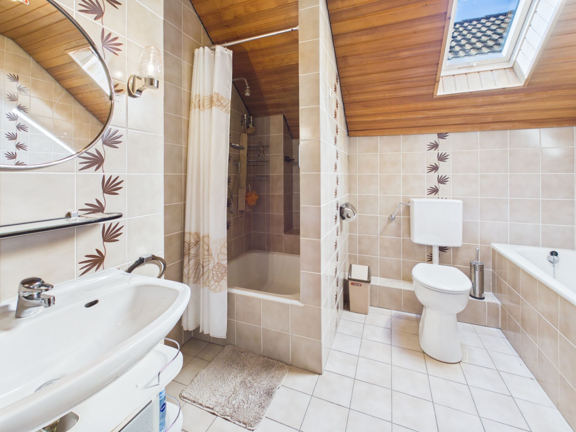 Badezimmer mit Badewanne, Dusche, Toilette, Waschbecken und Dachfenster unter Holzdecke.