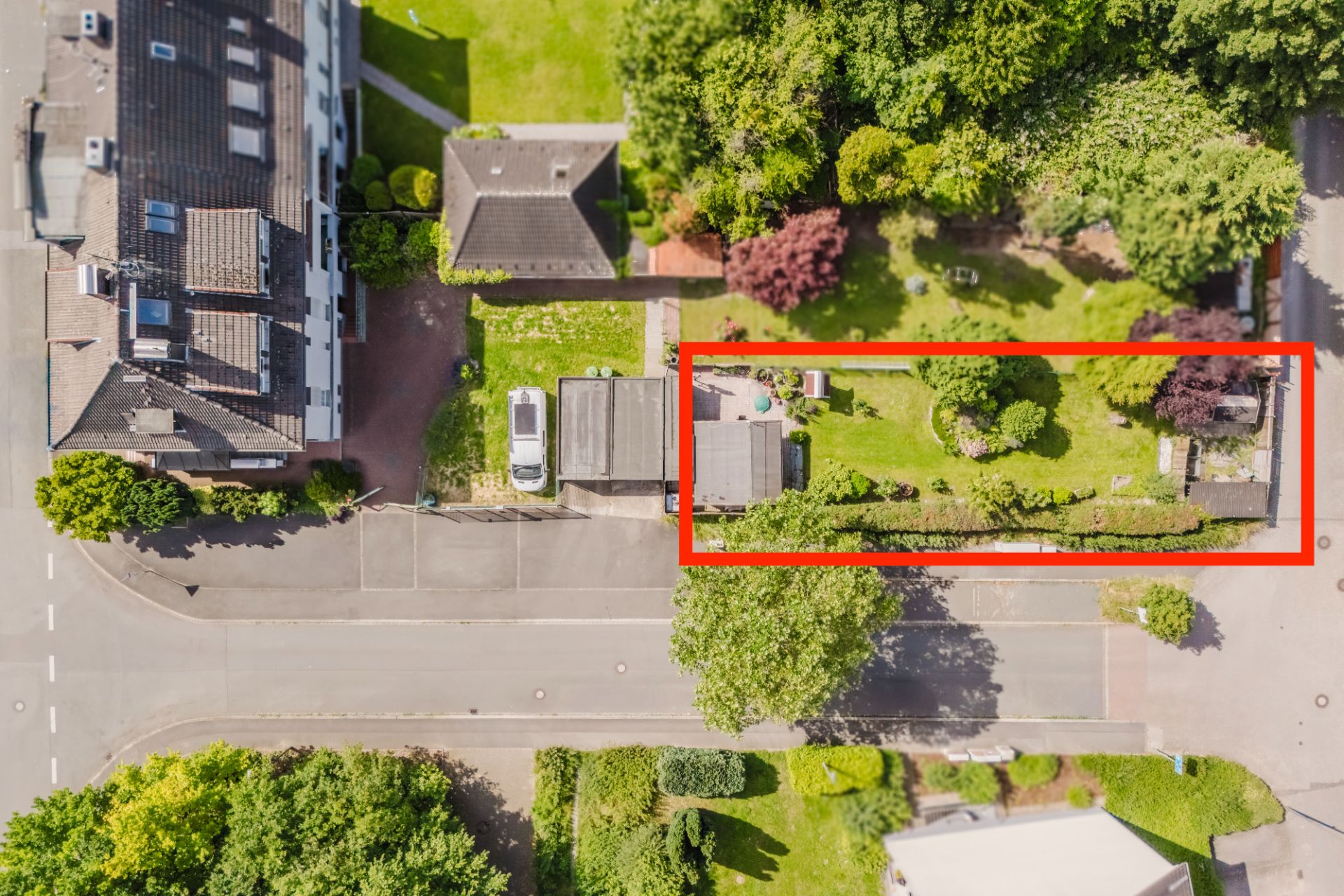 Luftaufnahme eines rechteckigen Gartengrundstücks mit Haus, Rasen und Bäumen, rot markiert.