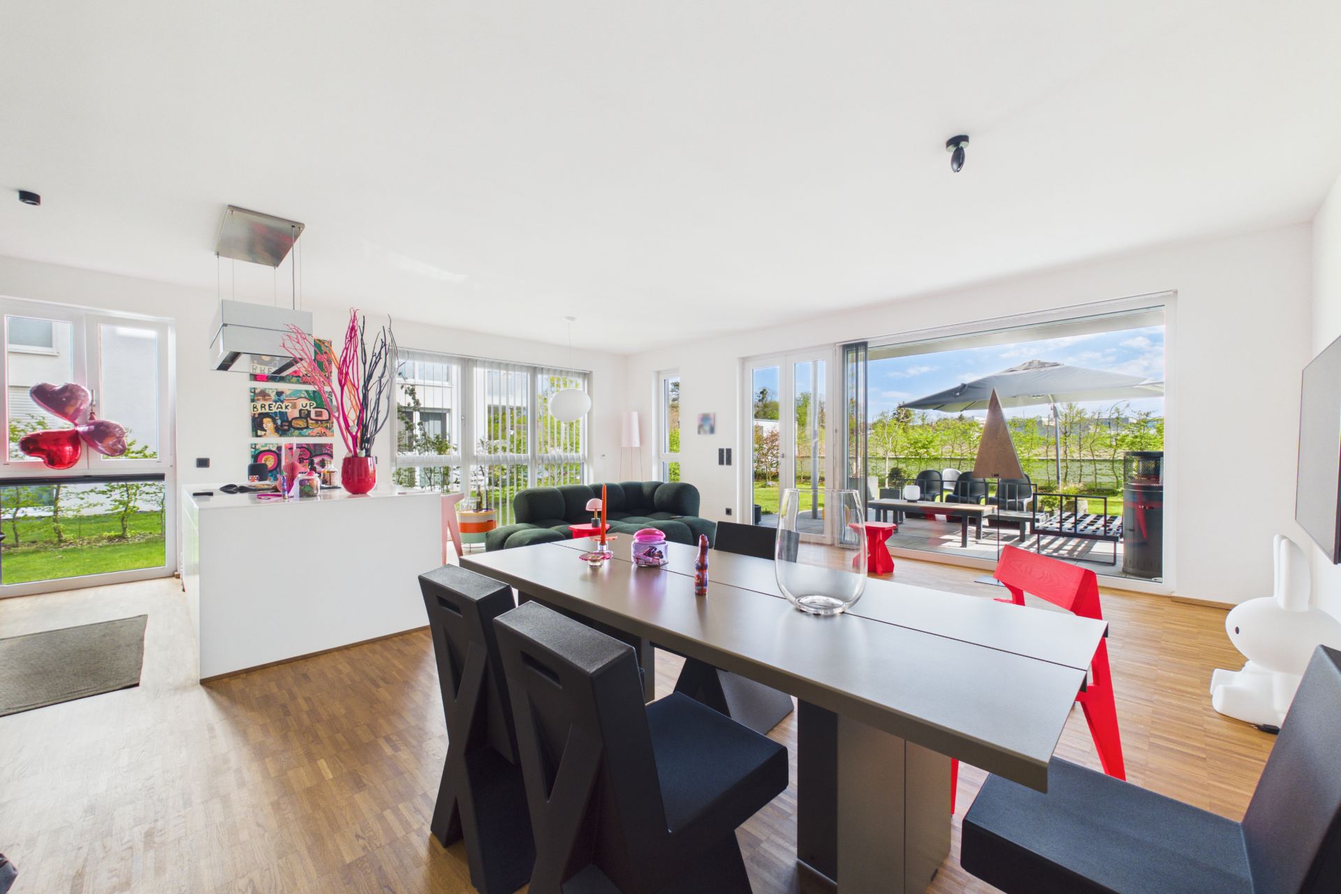 Helles Wohnzimmer mit Esstisch, Stühlen, Sofa und Zugang zur Terrasse mit Sonnenschirm.