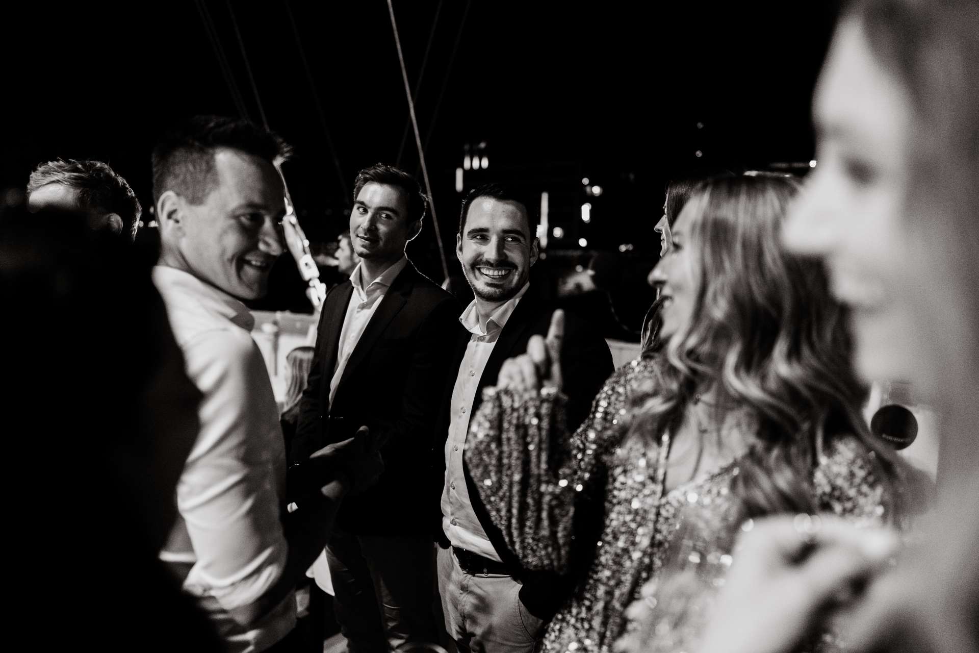 Mehrere Menschen unterhalten sich lachend bei Nacht, einige tragen festliche Kleidung.
