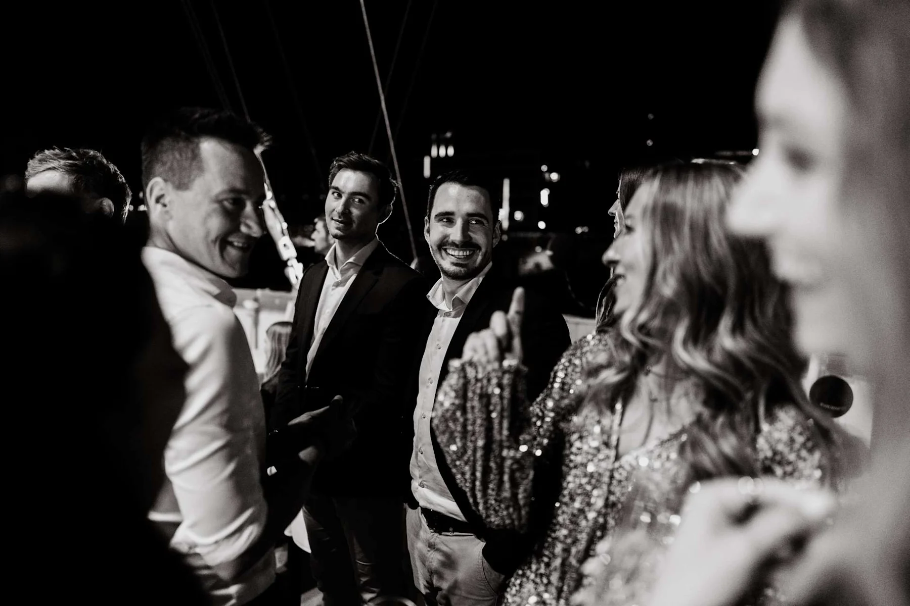 Mehrere Menschen unterhalten sich lachend bei Nacht, einige tragen festliche Kleidung.