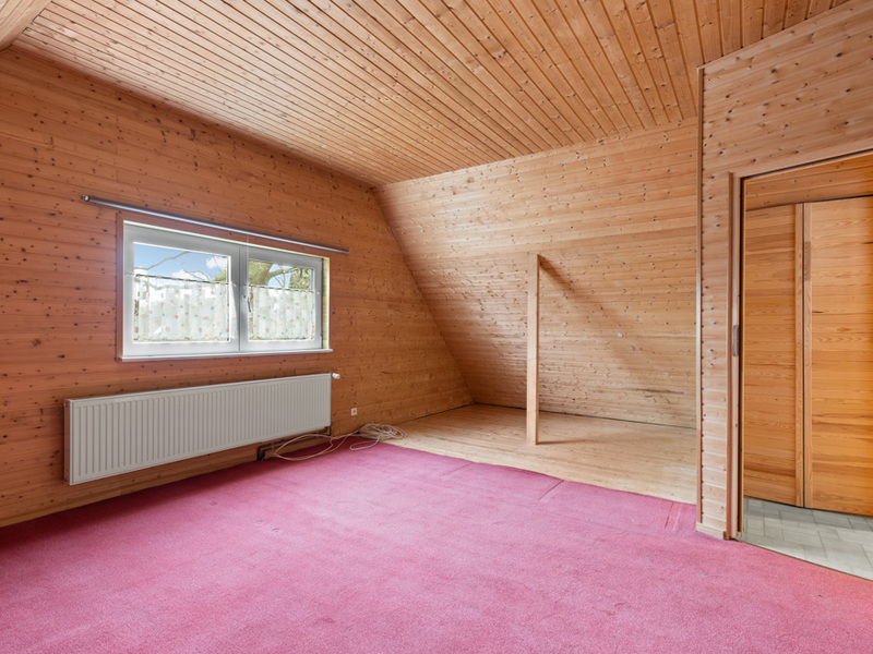 Leeres Zimmer mit Holzverkleidung, Fenster, Heizkörper und rotem Teppichboden.