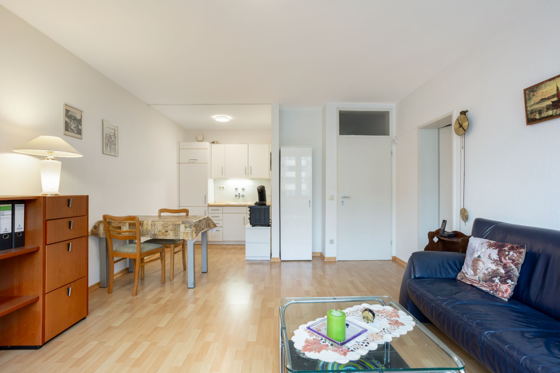 Helles Wohnzimmer mit blauer Couch, Tisch, Essbereich und offener Küche.
