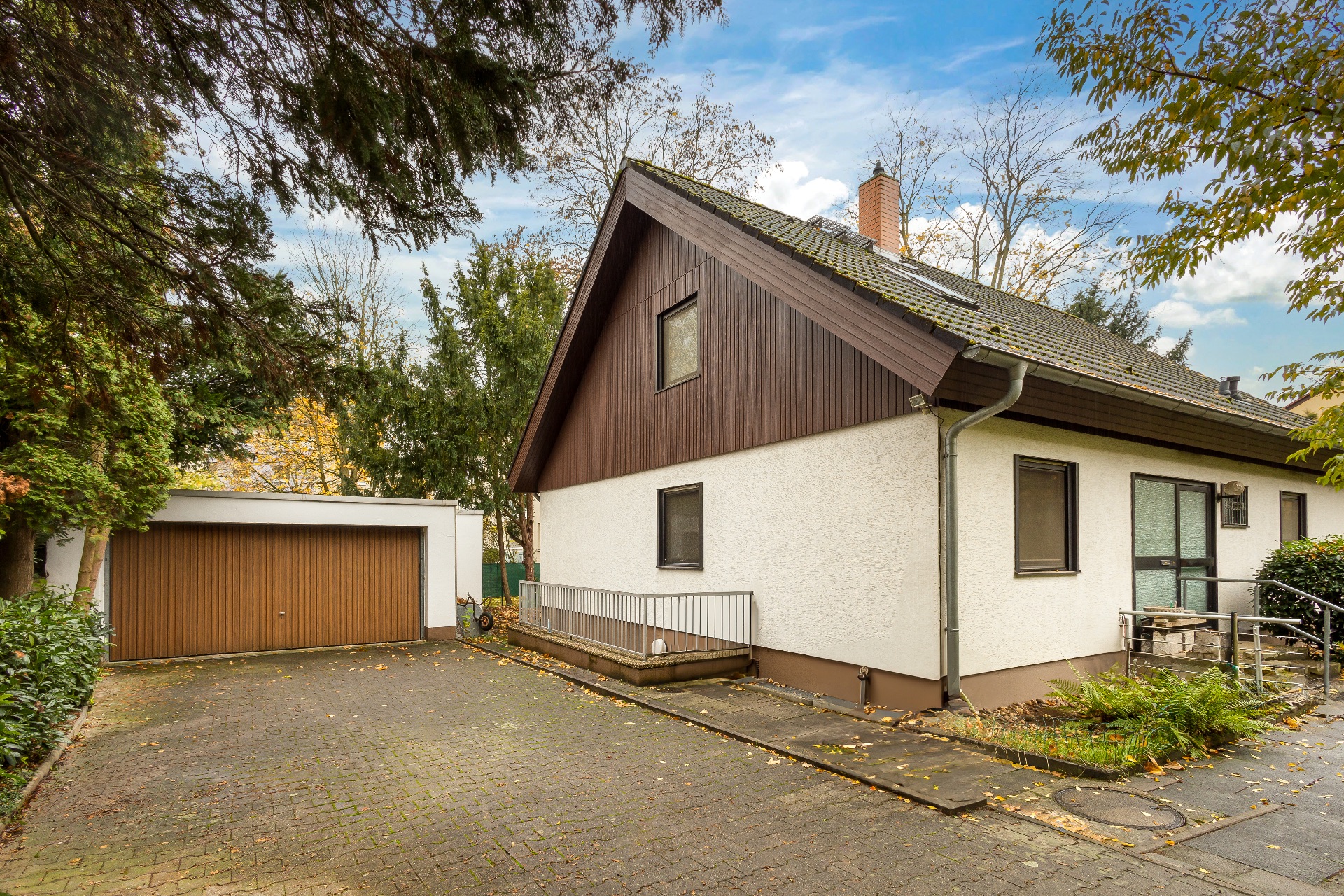 Einfamilienhaus mit Satteldach und angrenzender Garage, umgeben von Bäumen.