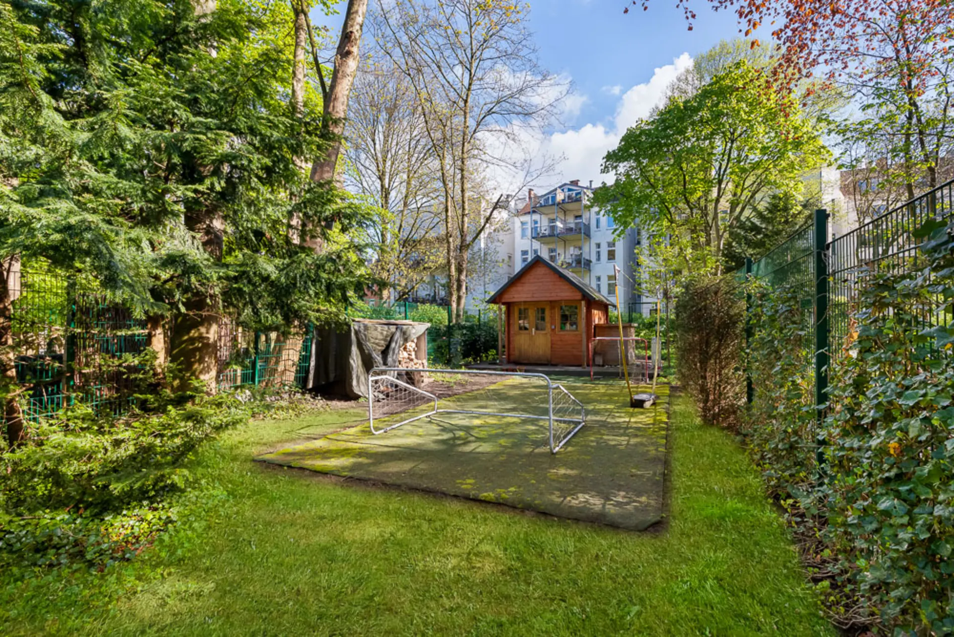 Garten mit kleinem Fußballtor, grünem Rasen und Holzhaus im Hintergrund.