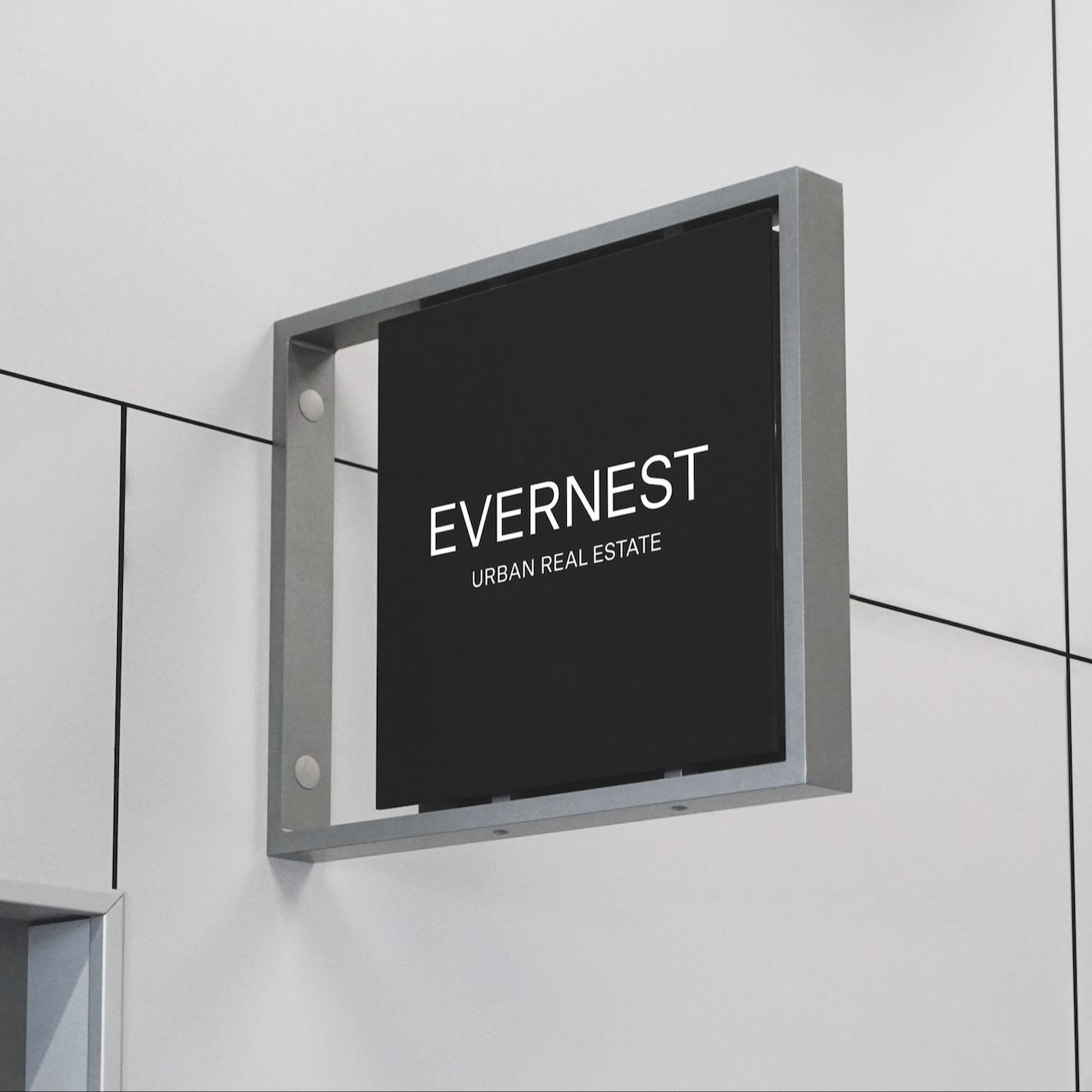 Schwarzes Firmenschild mit der Aufschrift 'EVERNEST URBAN REAL ESTATE' an einer weißen Wand.