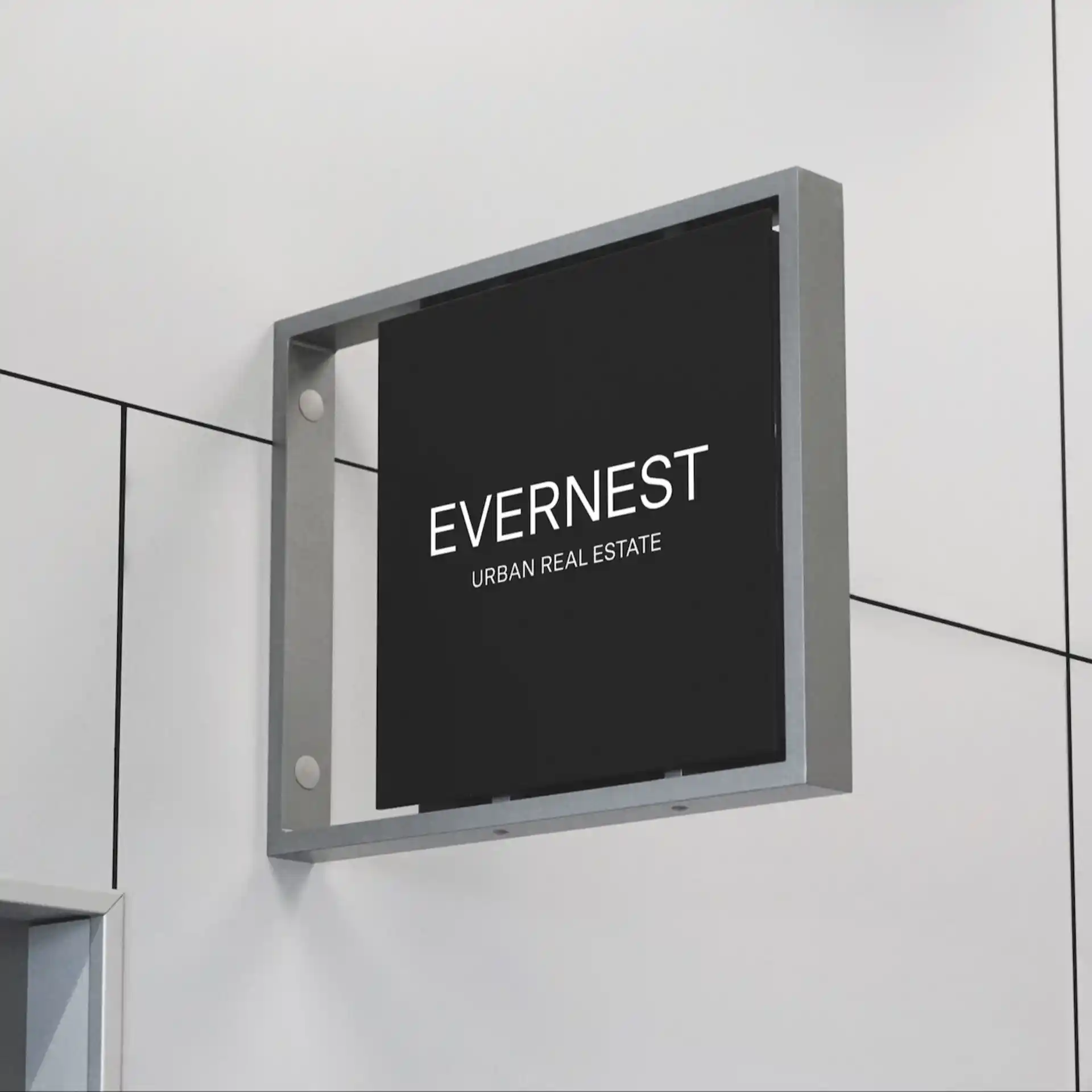 Schwarzes Firmenschild mit der Aufschrift 'EVERNEST URBAN REAL ESTATE' an einer weißen Wand.