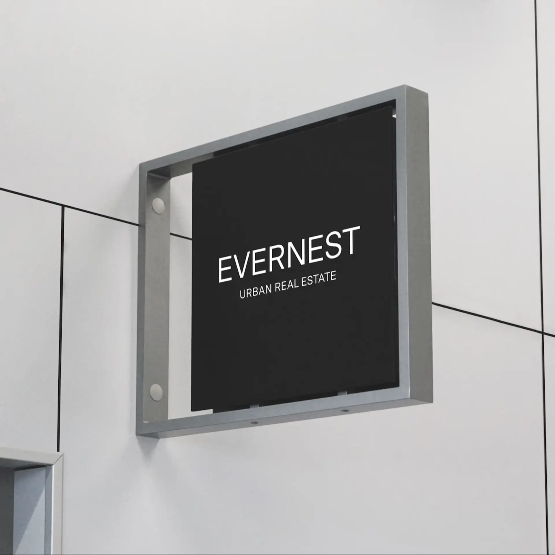 Schwarzes Firmenschild mit der Aufschrift 'EVERNEST URBAN REAL ESTATE' an einer weißen Wand.