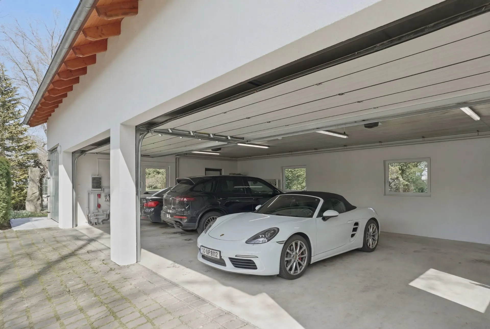 Dreifachgarage mit zwei Autos und einem Cabrio, helle Wände und Fenster, Garagentore offen.