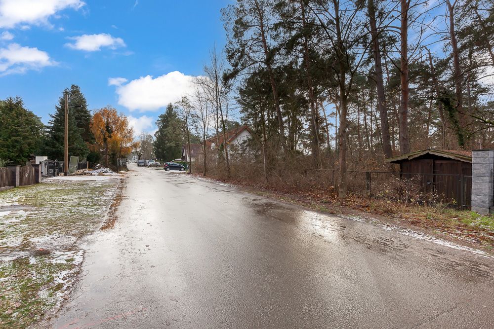 Nasse Wohnstraße mit Bäumen, einigen Autos und Häusern am Straßenrand.