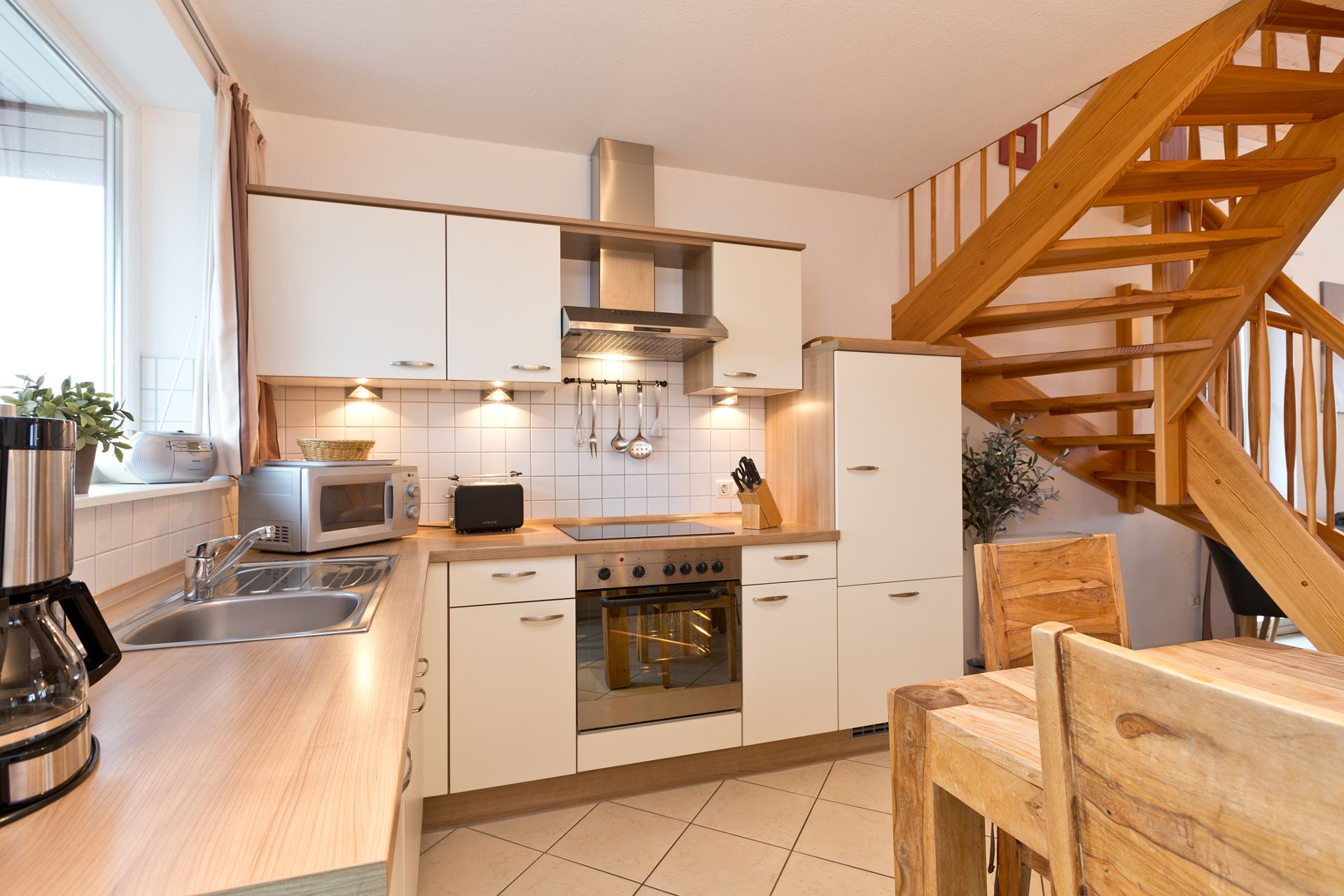 Moderne Einbauküche mit Holztreppe und Esstisch aus Holz in heller Wohnumgebung.