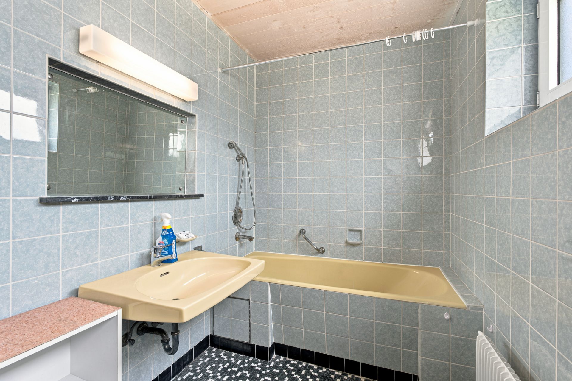 Badezimmer mit gelber Badewanne, Waschbecken, Spiegel und blauen Fliesen an den Wänden.
