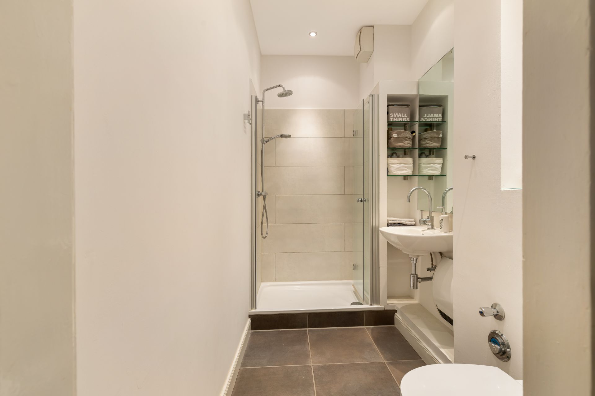 Modernes Badezimmer mit Dusche, Waschbecken, Regalen mit Handtüchern und WC.