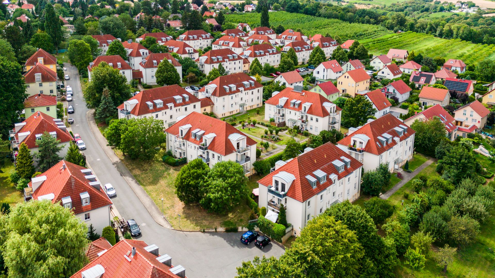 Luftaufnahme eines Wohngebiets mit weißen Häusern und roten Dächern, umgeben von Bäumen.