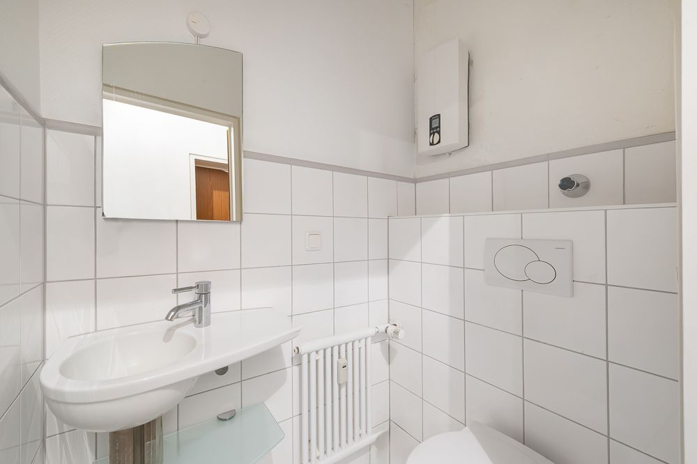 Kleines, gefliestes Bad mit Waschbecken, Spiegel, Toilette und Heizkörper.