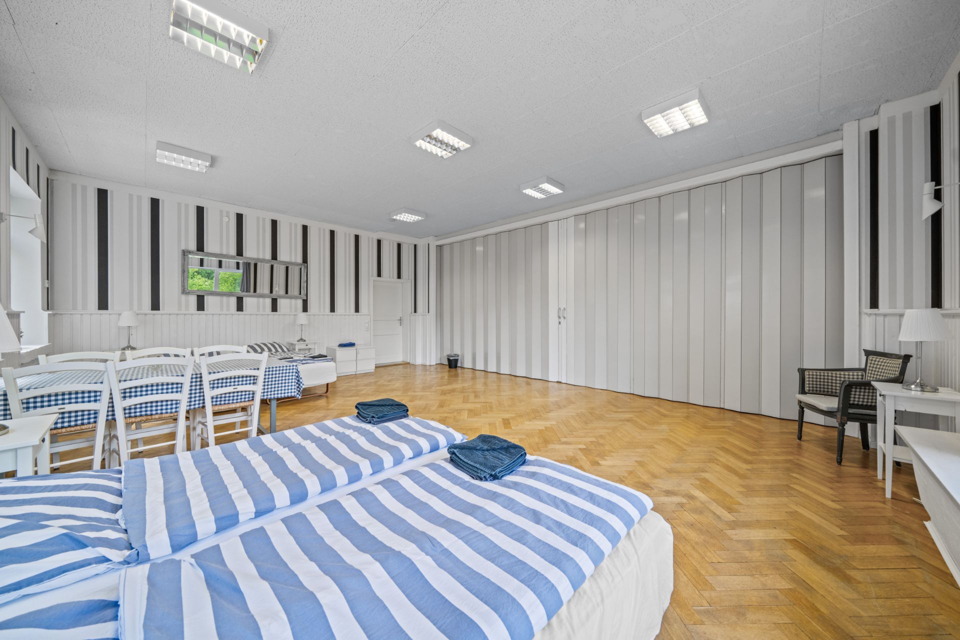 Großes Schlafzimmer mit zwei Betten, gestreifter Bettwäsche und Parkettboden, Schreibtisch sowie Stühlen.