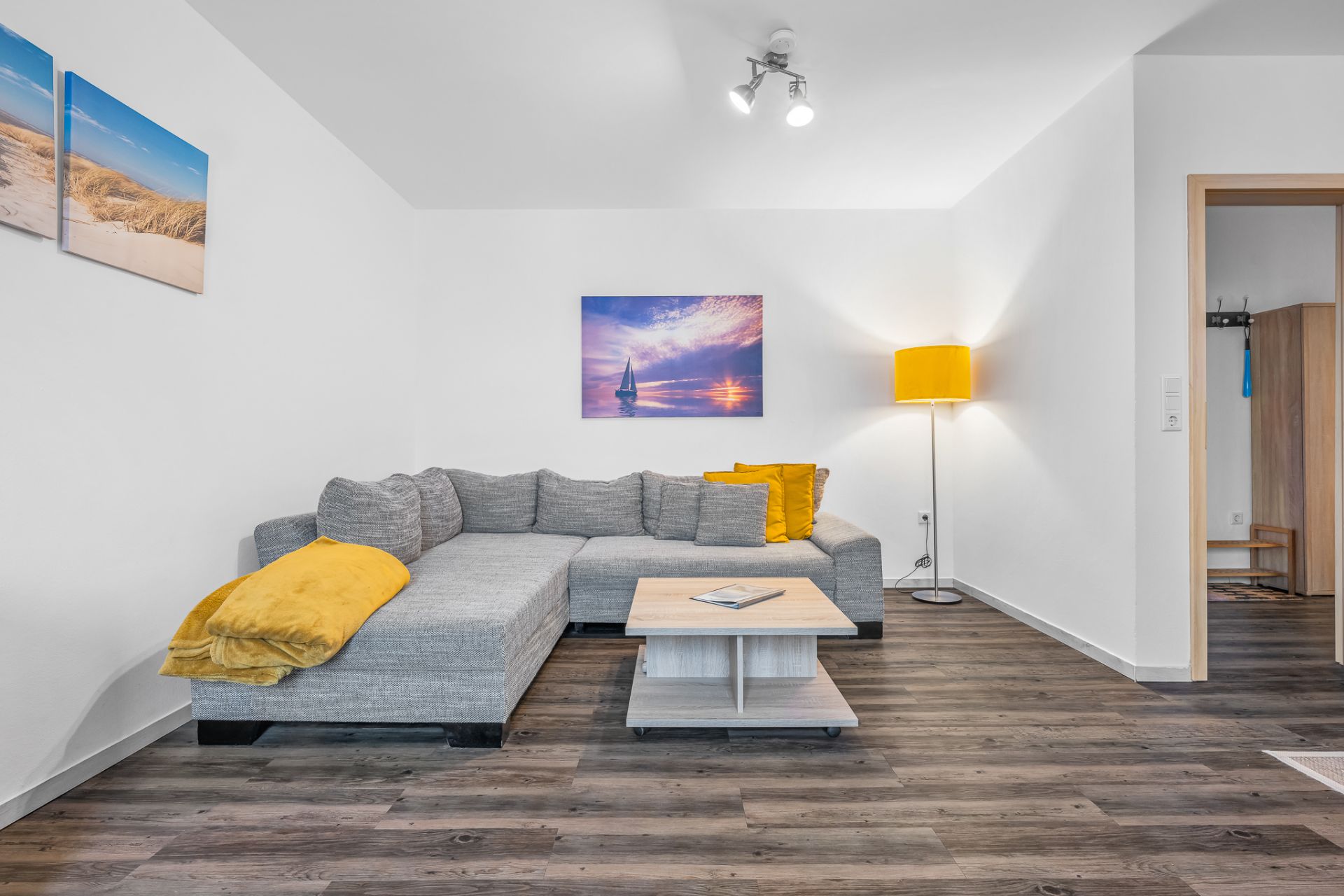 Helles Wohnzimmer mit grauem Ecksofa, Couchtisch, Stehlampe und Wandbildern.