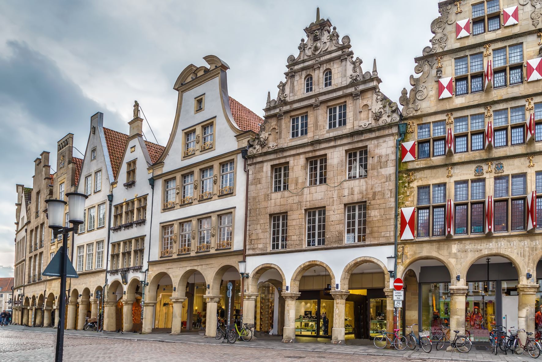 Reihe historischer Wohngebäude mit Bögen und vielen Fenstern an einer gepflasterten Straße.