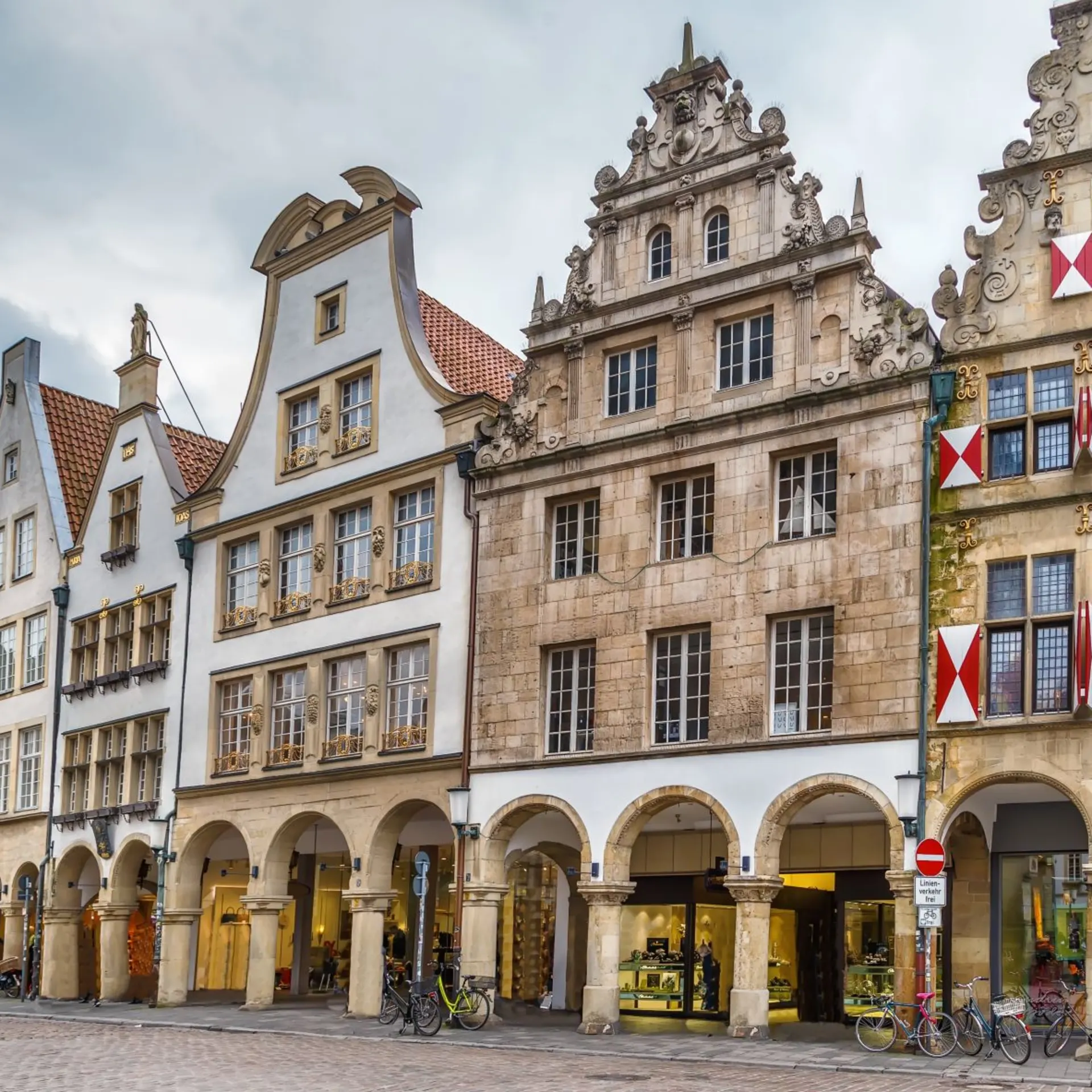 Reihe historischer Wohngebäude mit Bögen und vielen Fenstern an einer gepflasterten Straße.