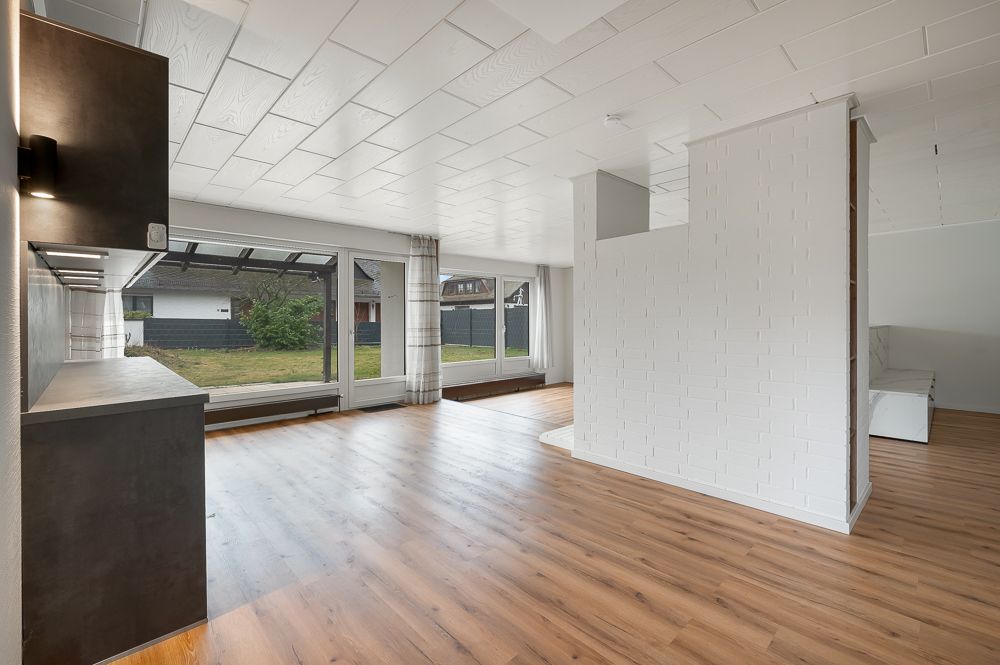 Helles Wohnzimmer mit großen Fenstern, Holzboden und halbhoher weißer Trennwand.