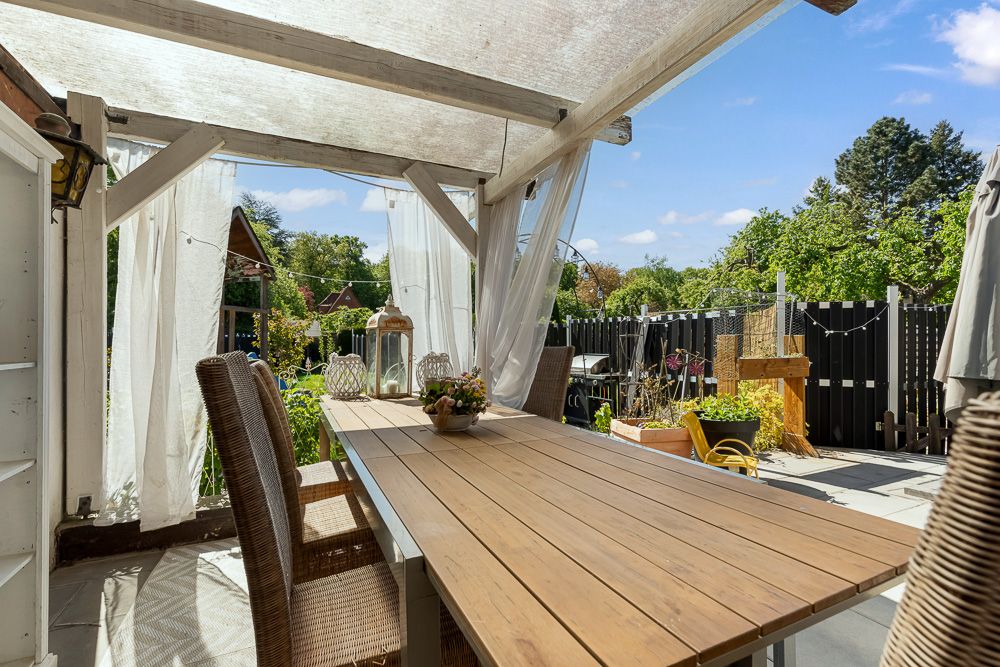 Überdachte Terrasse mit Holztisch, Stühlen und Blick auf einen Garten.