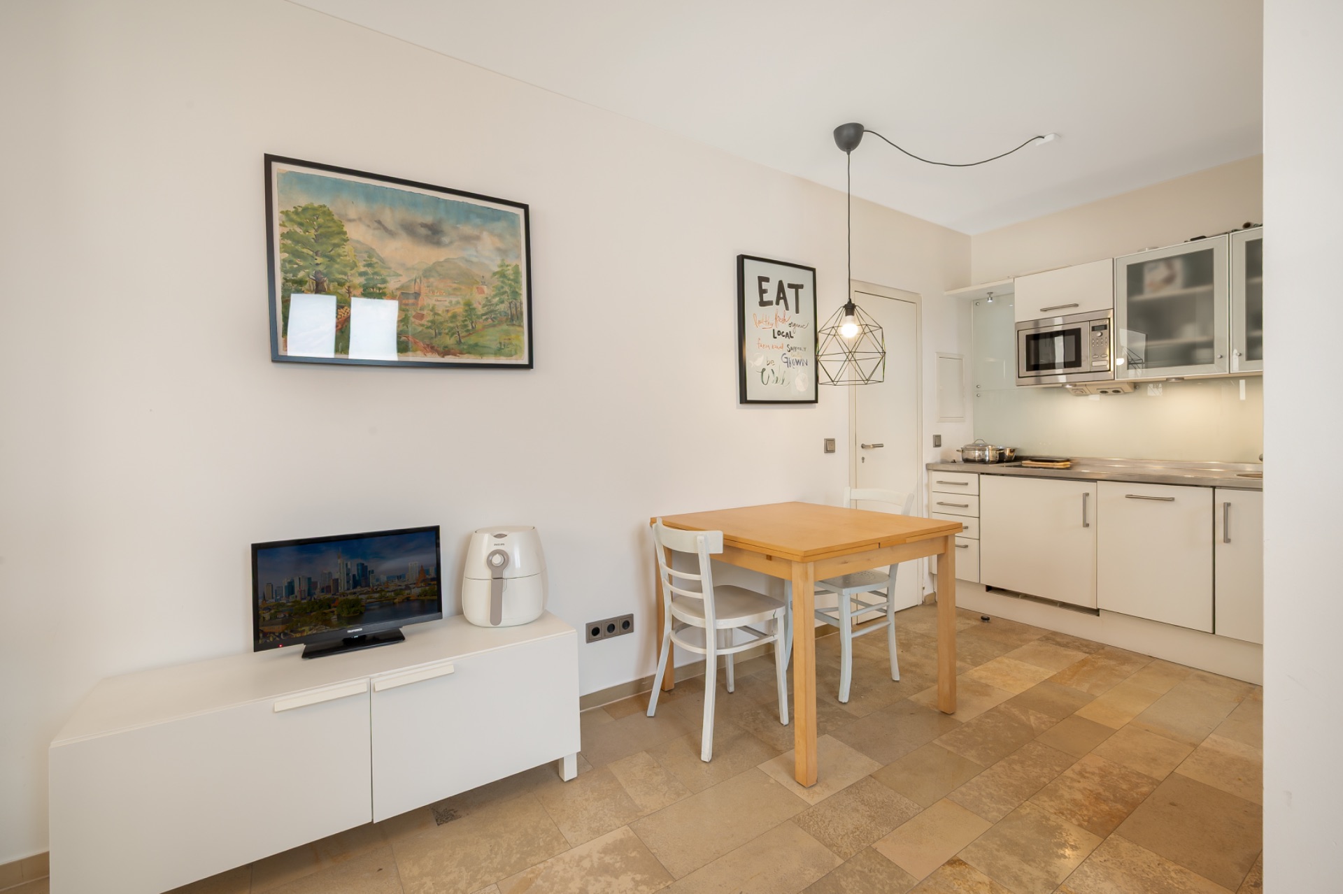 Kleine Wohnküche mit Esstisch, Stühlen, Sideboard, Bildern und moderner Einbauküche.