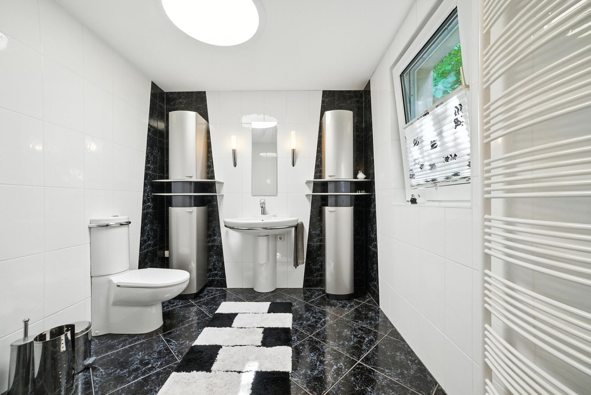 Modernes Badezimmer mit schwarzem Fliesenboden, WC, Waschbecken, Spiegel und Fenster.