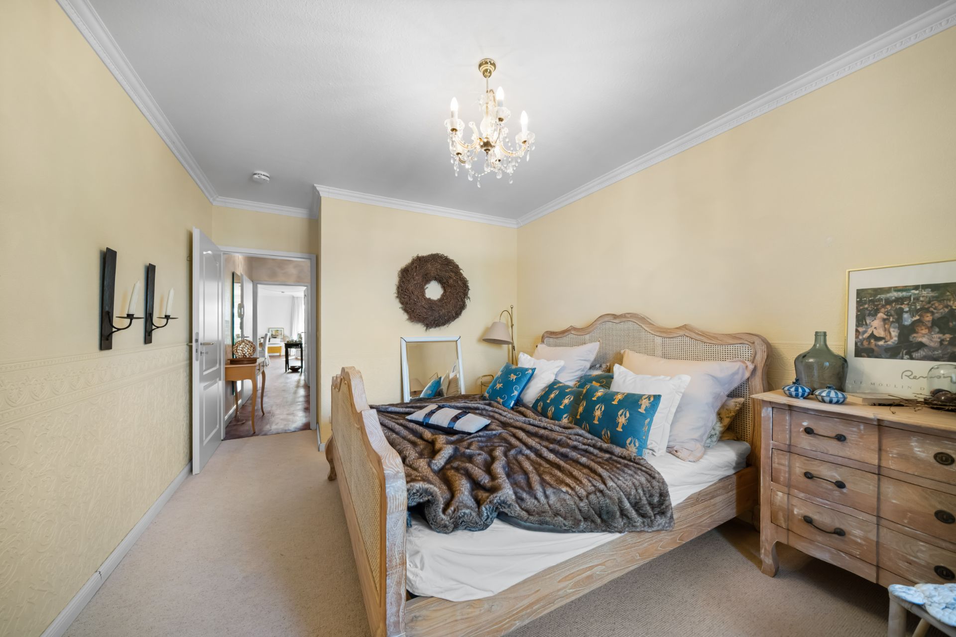 Schlafzimmer mit Doppelbett, Holzmöbeln, Kronleuchter und gelben Wänden.