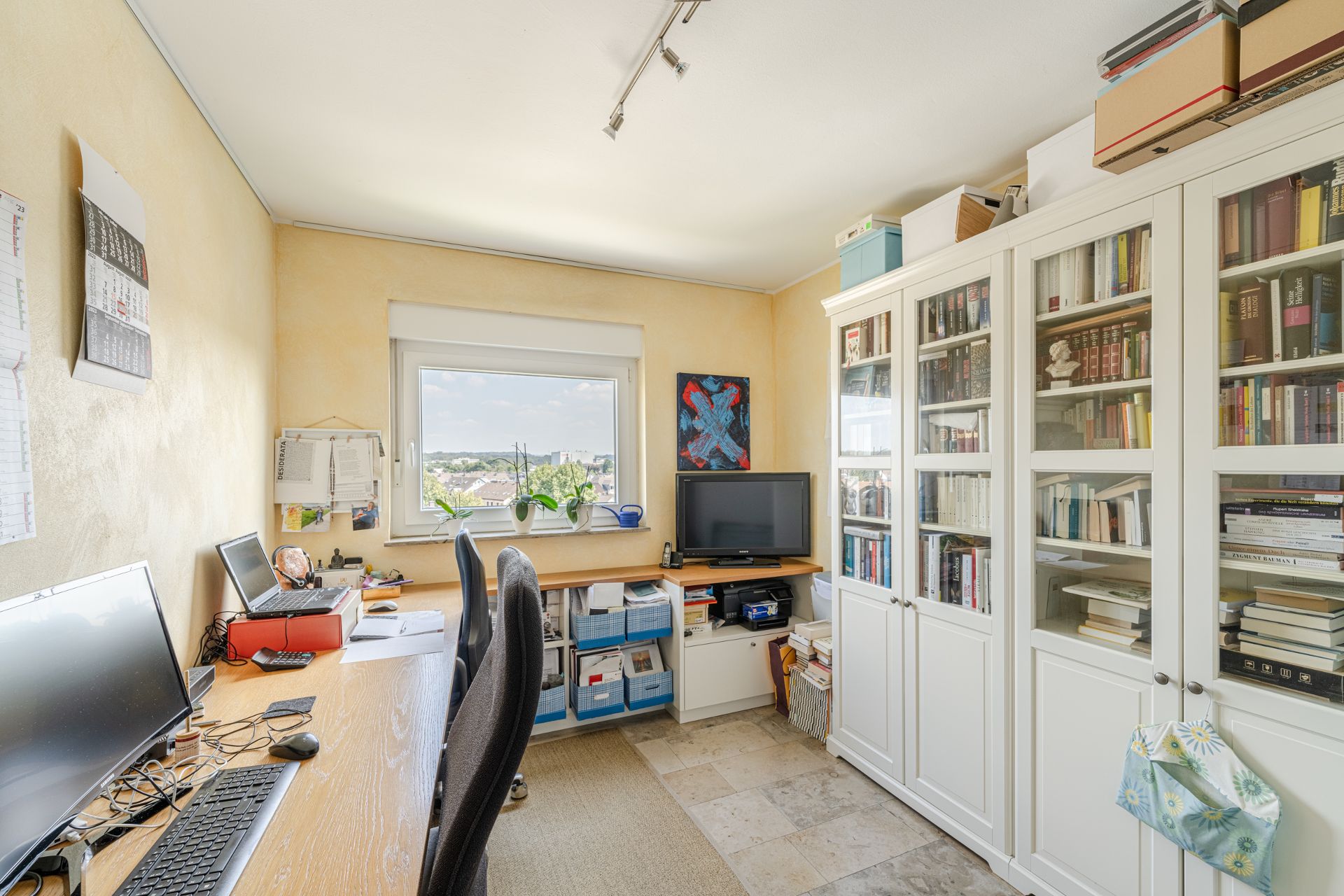 Helles Arbeitszimmer mit Schreibtisch, Computer, Bücherregalen und Fenster mit Ausblick.