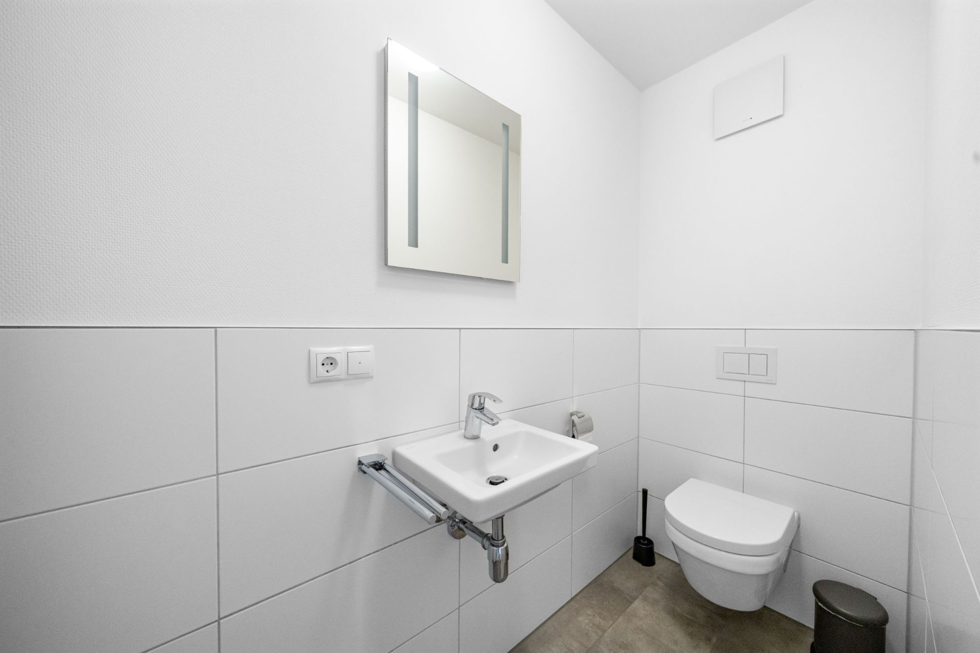 Modernes, weiß gefliestes Badezimmer mit Spiegel, Waschbecken und Wandtoilette.