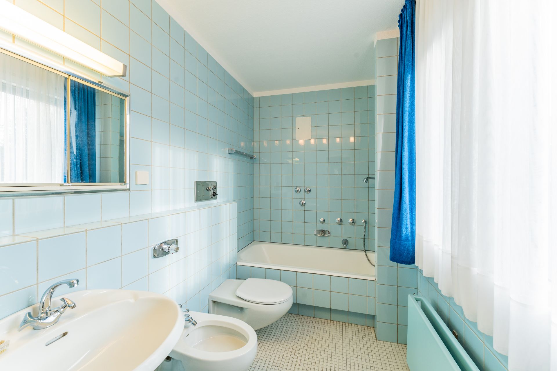 Helles Badezimmer mit blauen Fliesen, Badewanne, Waschbecken, Toilette und Bidet.