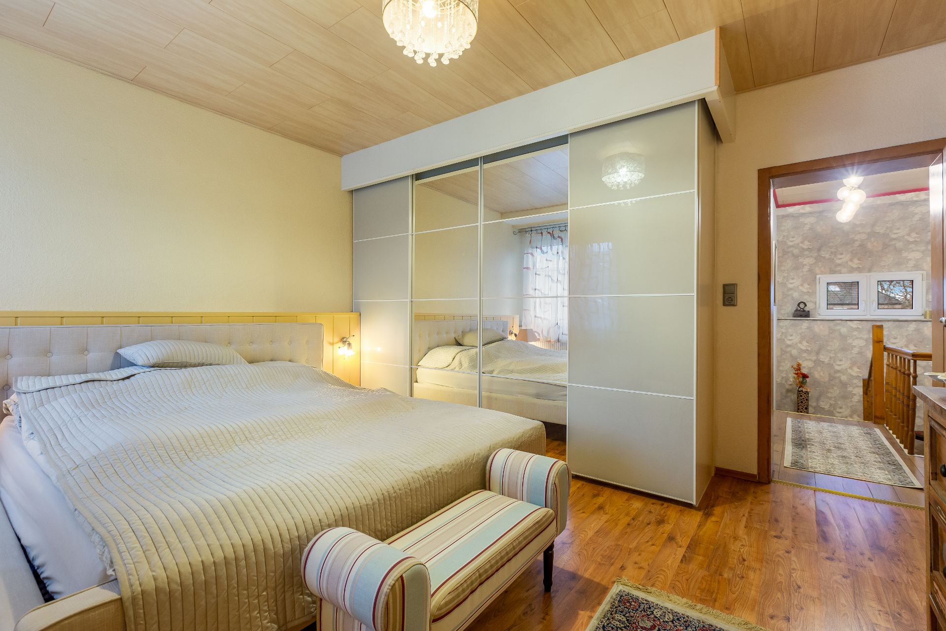 Schlafzimmer mit großem Bett, Spiegel-Kleiderschrank, Holzfußboden und Deckenlampe.