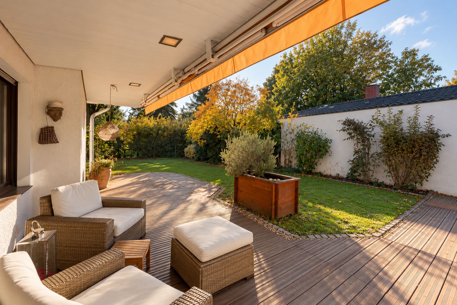 Überdachte Terrasse mit Sitzmöbeln und Blick auf Garten mit Rasen und Bäumen.