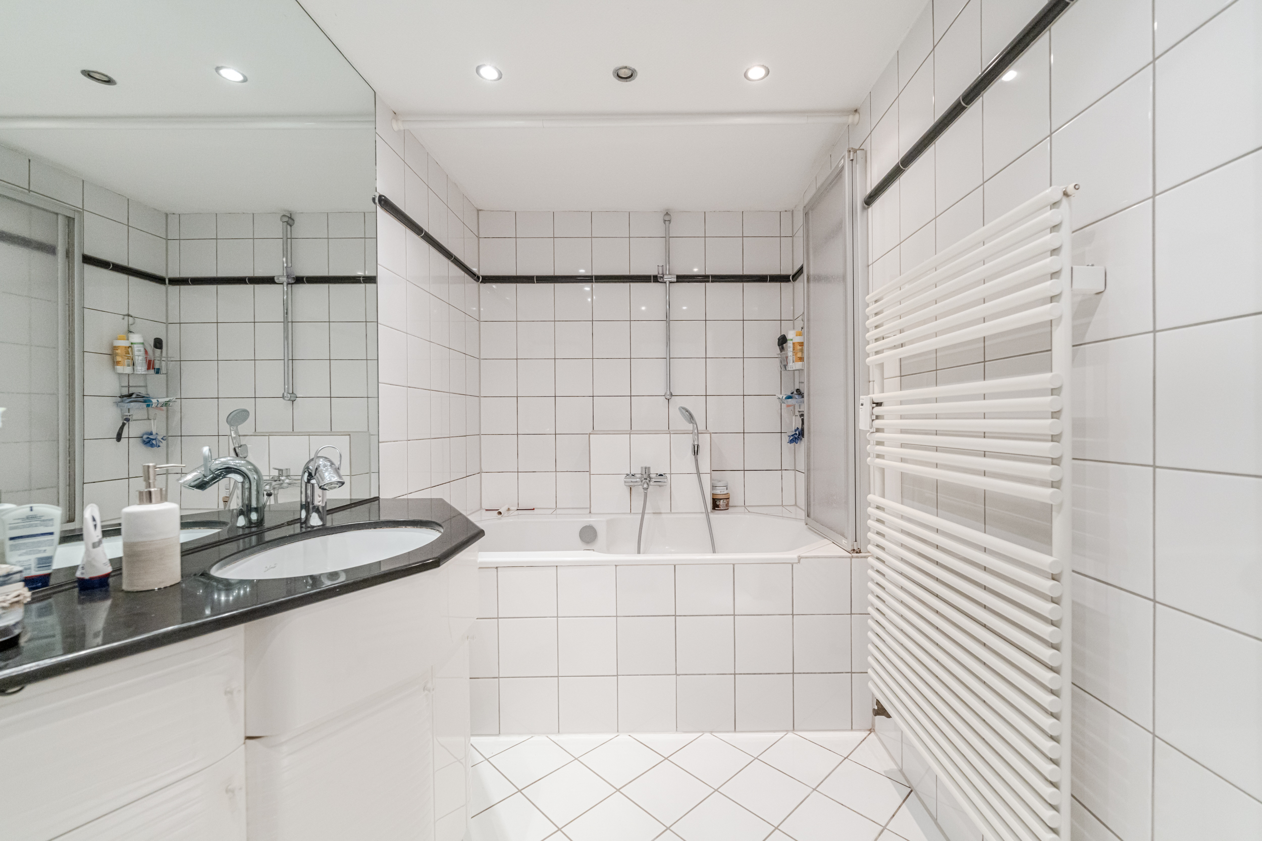 Helles Badezimmer mit weiß gefliesten Wänden, Badewanne, Waschbecken und Handtuchheizkörper.