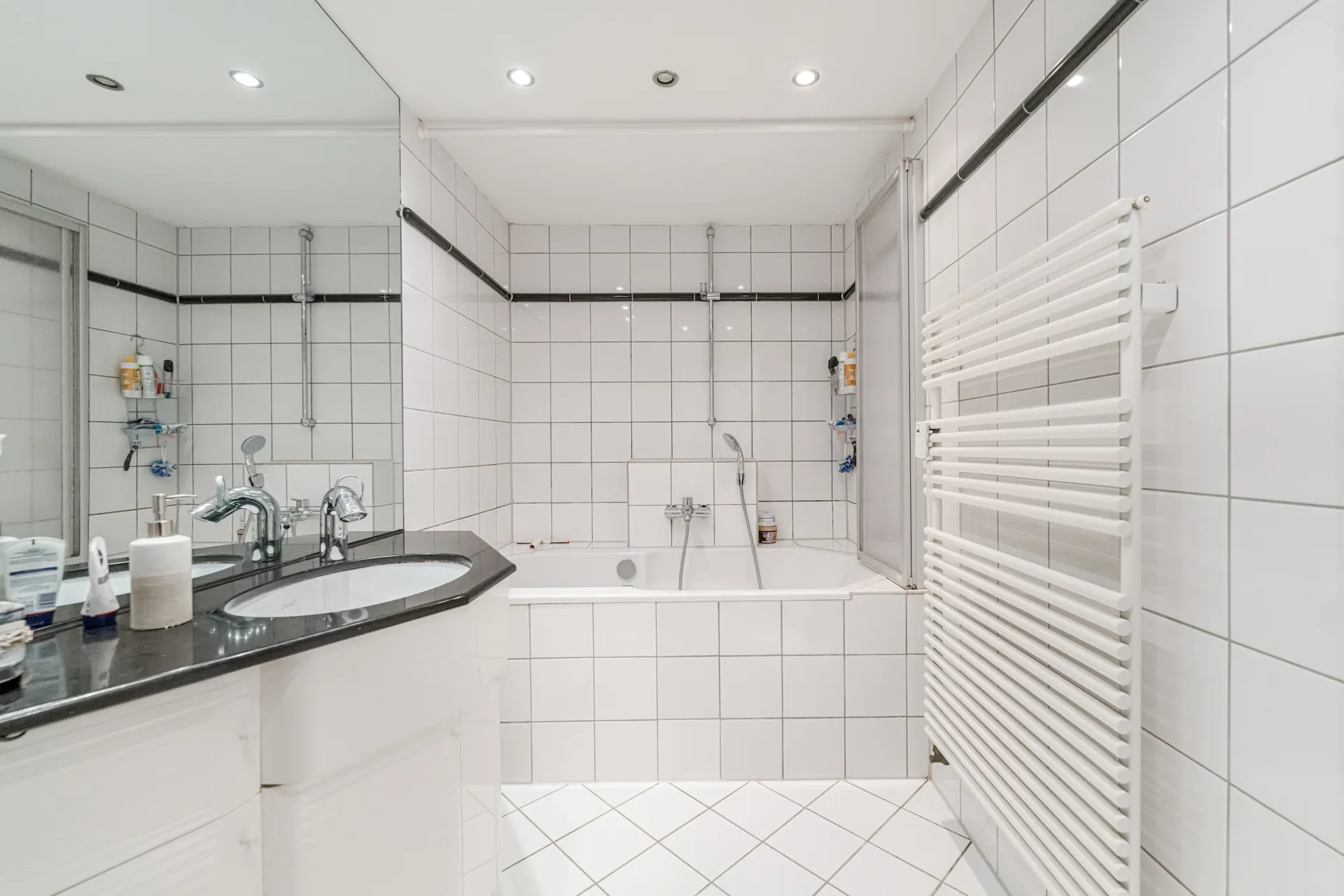 Helles Badezimmer mit weiß gefliesten Wänden, Badewanne, Waschbecken und Handtuchheizkörper.