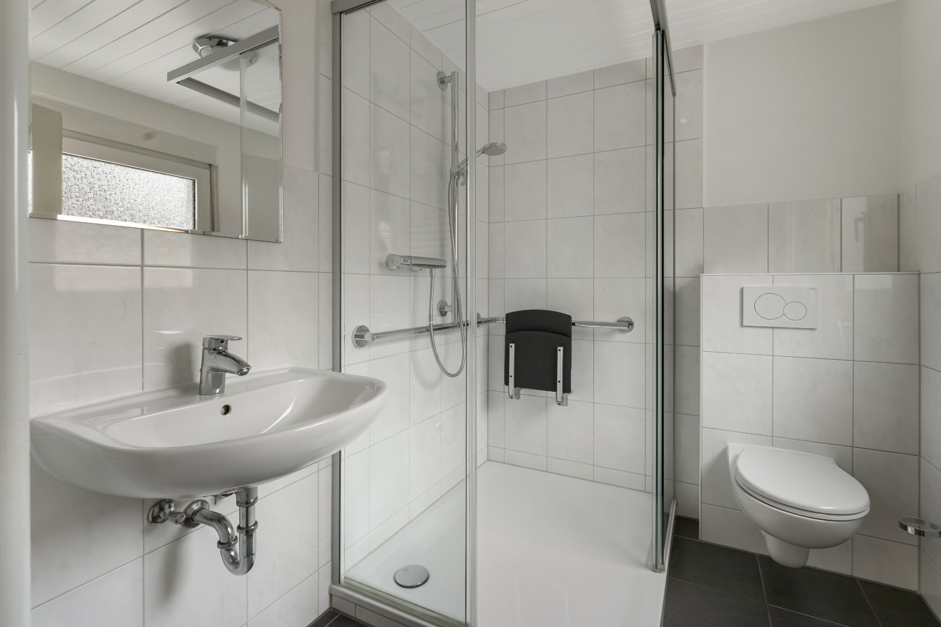 Modernes barrierefreies Bad mit Dusche, Waschbecken und Wand-WC, alles in Weiß gehalten.