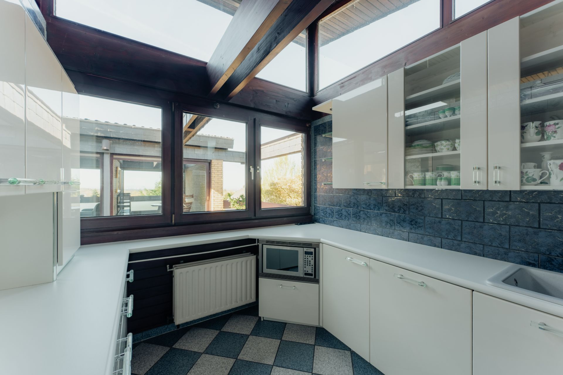 Helle, moderne Küche mit weißen Schränken, Eckfenster und Fliesenboden.