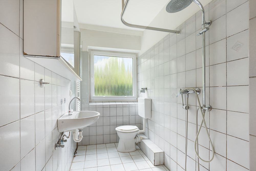 Helles Badezimmer mit weiß gefliesten Wänden, Toilette, Waschbecken und offener Dusche.