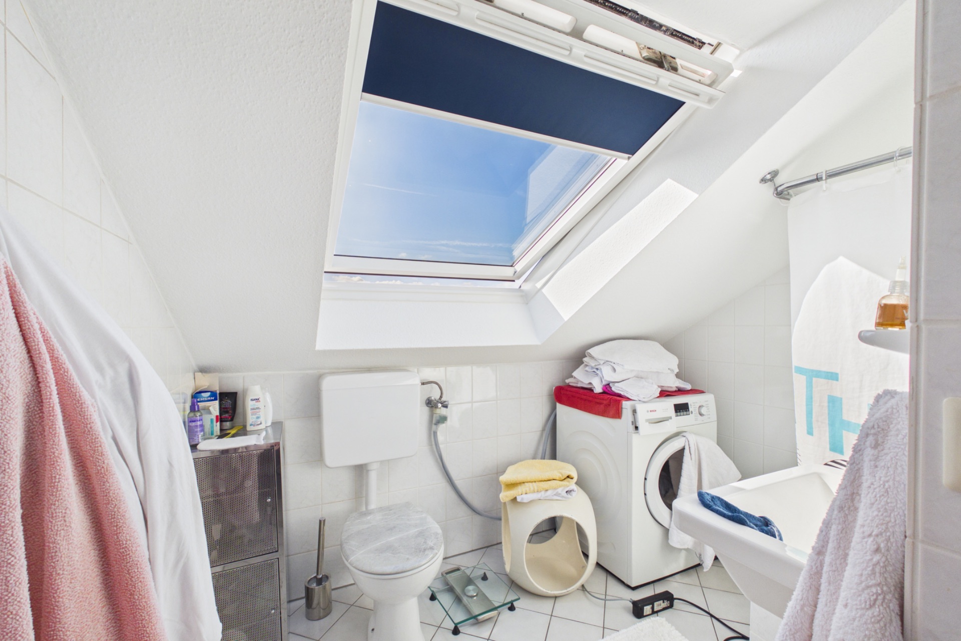 Helles Badezimmer mit Dachfenster, Toilette, Waschmaschine und Badewanne.