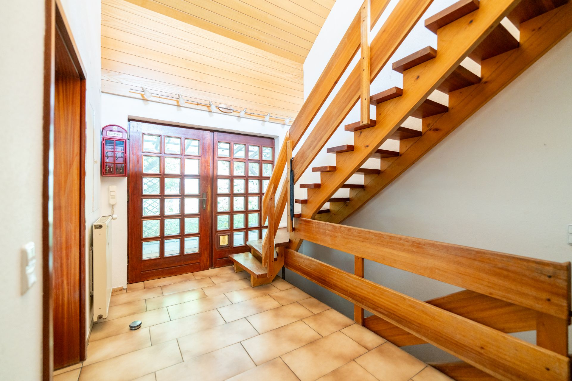 Heller Flur mit Holztreppe und Doppeltür mit Glasfenstern.