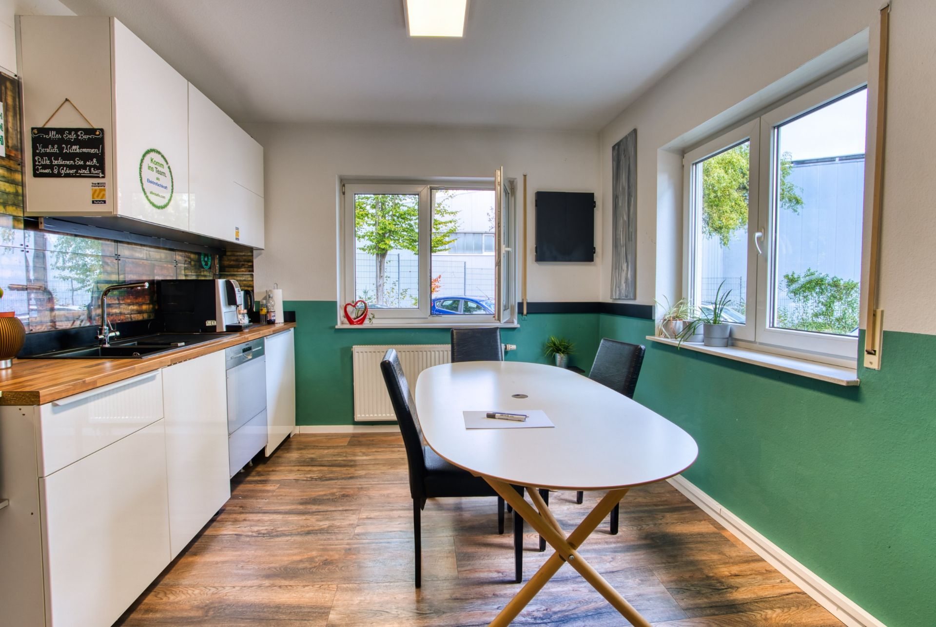 Moderne Küche mit Holzboden, Esstisch, Stühlen und großen Fenstern, viel Tageslicht.