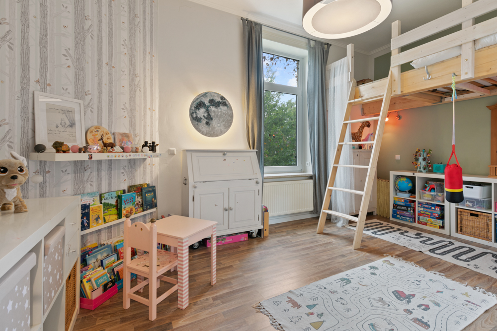 Helles Kinderzimmer mit Hochbett, Bücherregal, Spielzeug, Tisch und Stuhl auf Holzboden.