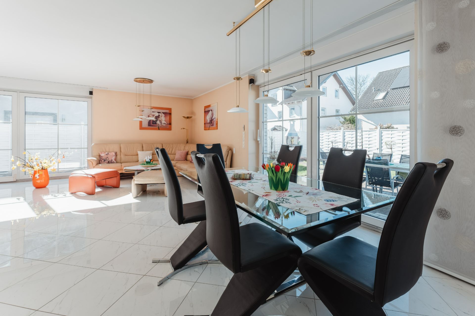 Helles Wohnzimmer mit Essbereich, Glastisch, schwarzen Stühlen und Blick auf Garten durch große Fenster.