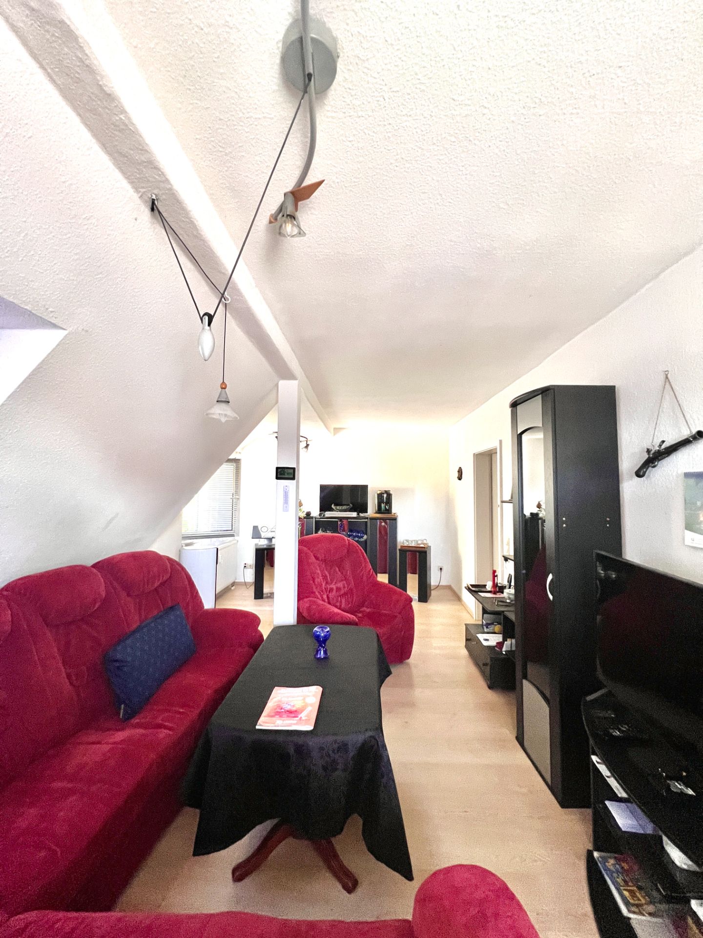 Wohnzimmer mit roten Sofas, schwarzem Couchtisch, Fernseher und hellen Holzböden.
