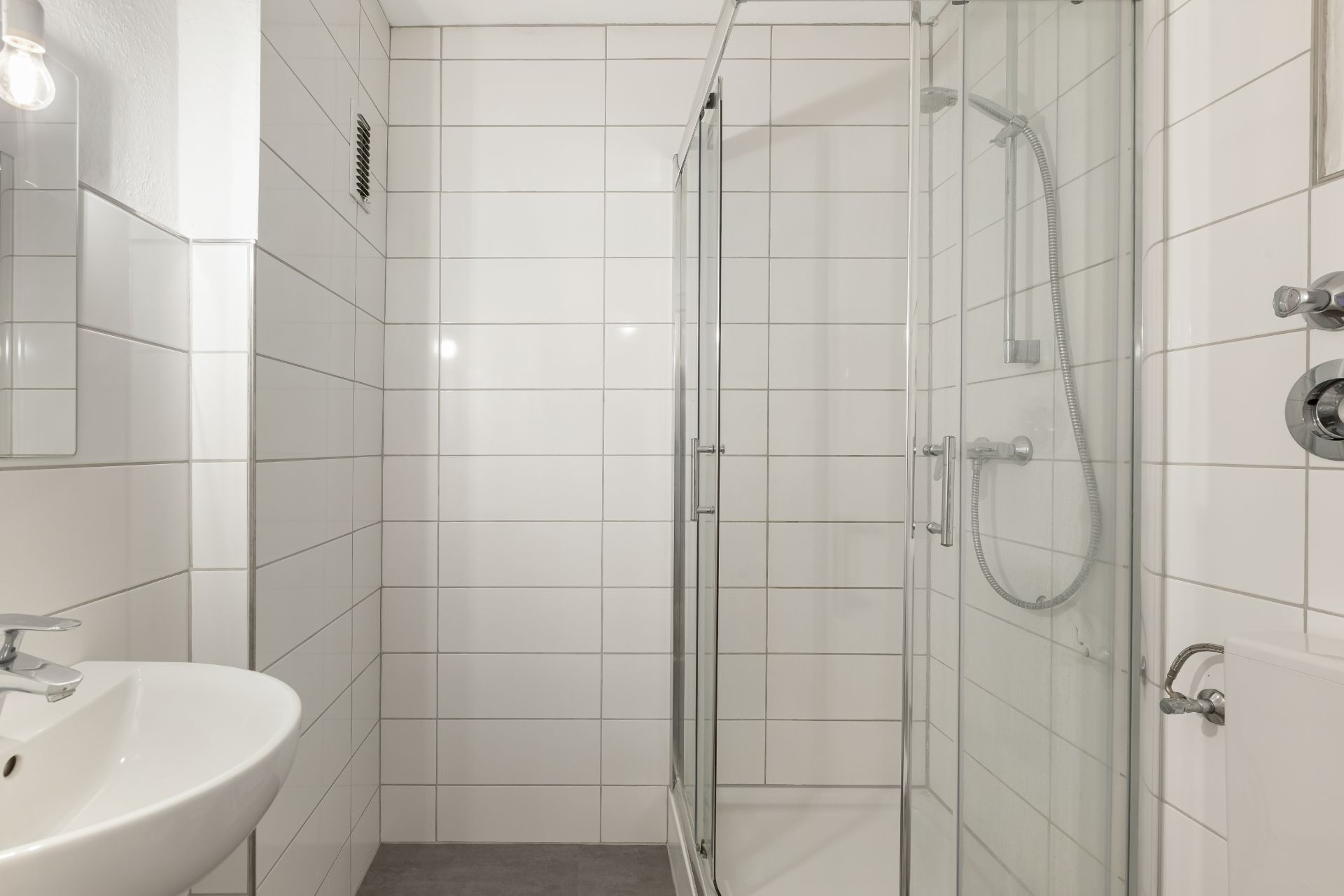 Helles Bad mit weiß gefliesten Wänden, Dusche mit Glastür und Waschbecken.