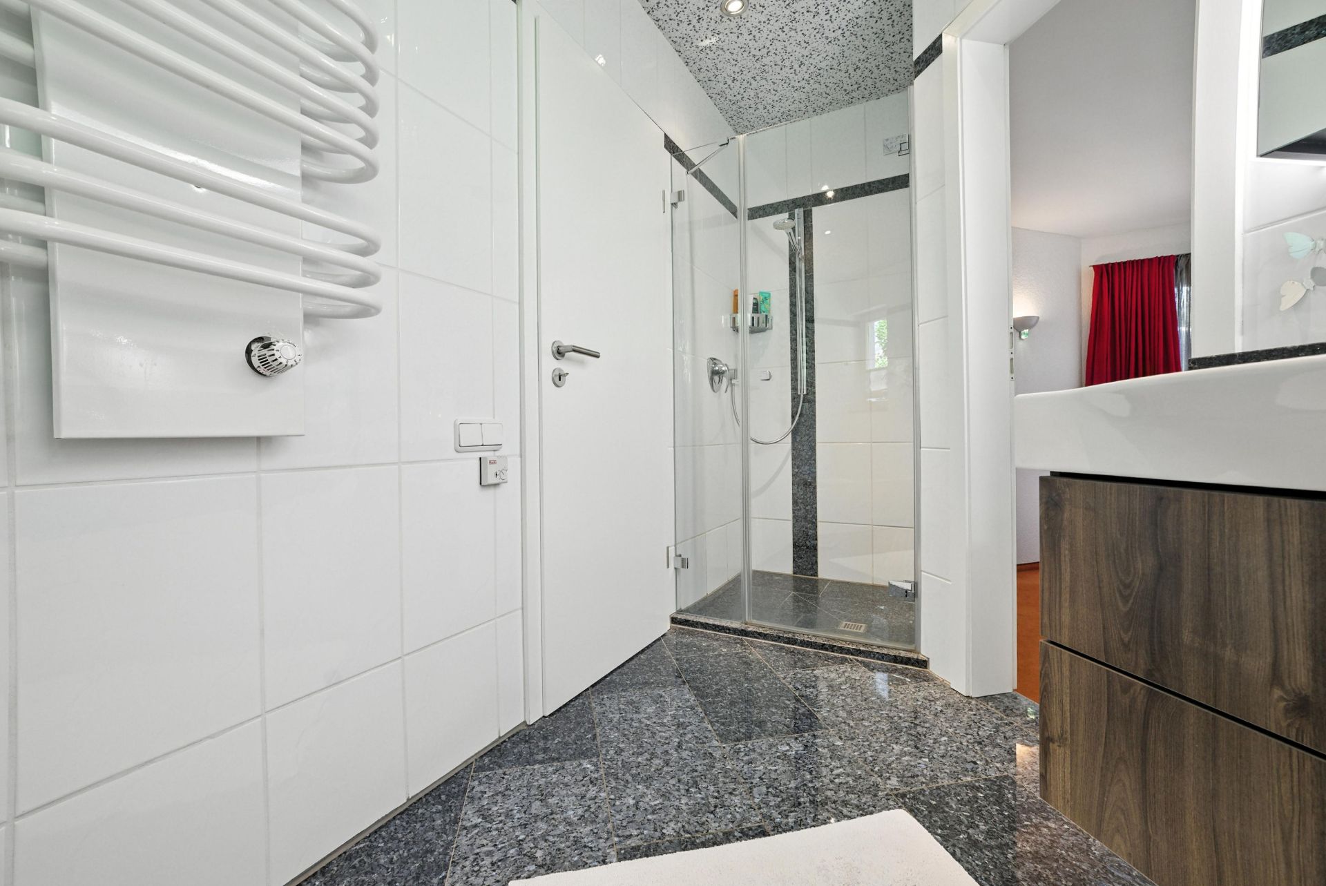 Modernes Badezimmer mit Dusche, weiß verfliesten Wänden und Handtuchheizkörper.